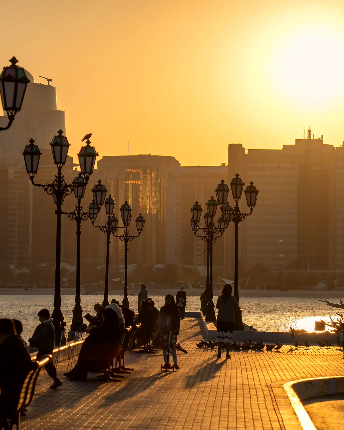 People walking along an Abu Dhabi waterfront promenade at sunset